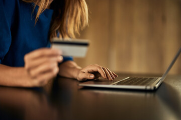 Side view of a woman entering data into the laptop, buying something online, and holding a credit...