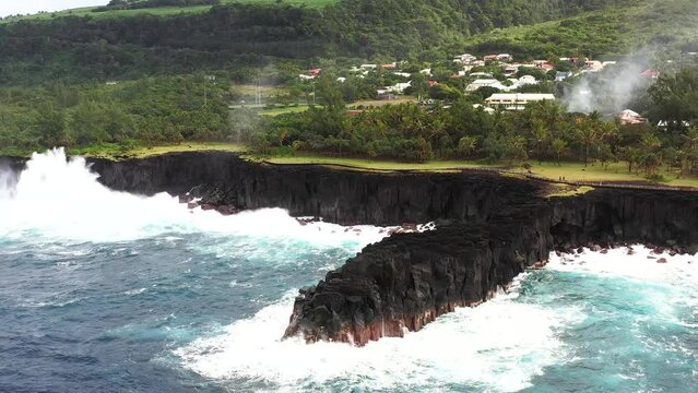 Aerial drone view of Puits des Francais on a stormy day with high breaking waves, cliffs and mountain range in the background, Saint-Philippe, Reunion.