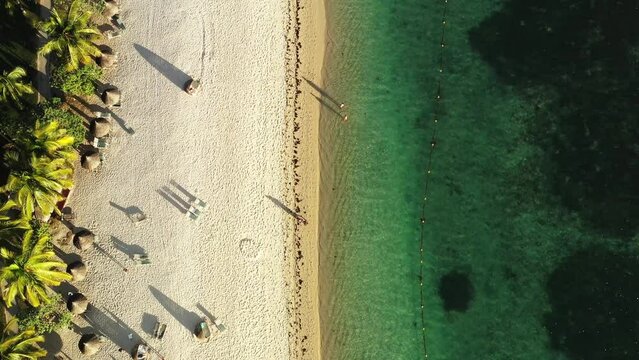 Aerial drone view of Flic en Flac beach at golden hour, with resorts, people, boats, deep hanging rain clouds and Mount Tourelle in the background, Flic en Flac, Black River, Mauritius.