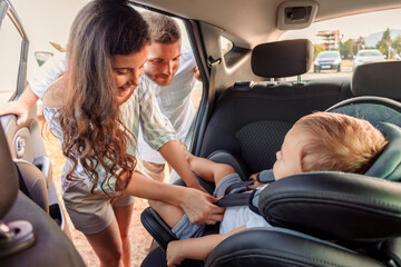 Parents fastening toddler son into a baby car seat