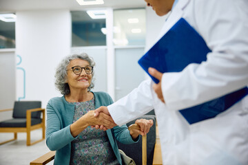 Happy senior woman greets her doctor in waiting room at medical clinic. - obrazy, fototapety, plakaty