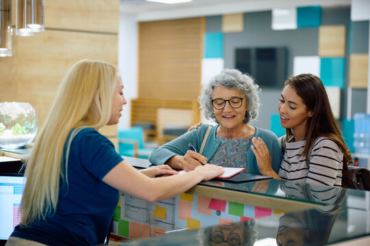 Happy senior woman checking in at doctor's office with help of her granddaughter, - Powered by Adobe