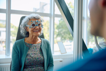 Happy elderly woman with optical testing glasses during eyesight exam at ophthalmologist.