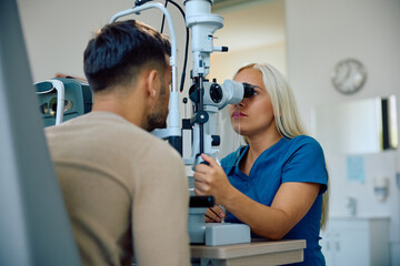 Female optometrist examining eyes of young patient at clinic.