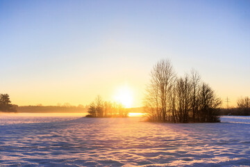 Snow-covered meadows in Siebenbrunn near Augsburg at sunrise with trees and bushes against a...