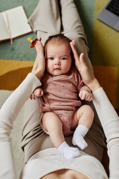 Top Down View Of Cute Baby Looking At Camera And Lying On Knees Of Mother Holding Baby Head With Pacifier In Hand