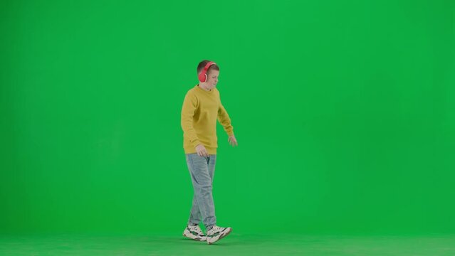 Portrait of boy on chroma key green screen. School boy kid in casual clothing in headphones walking and dancing, listening to music.