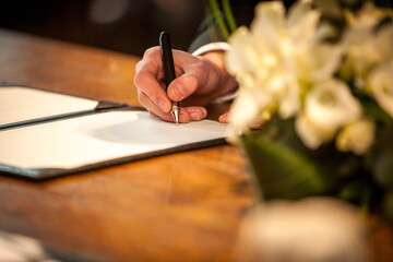 This image captures a close-up of a groom's hand as he signs the wedding register, a pivotal moment...