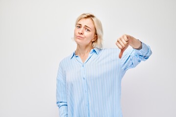 Portrait of blond girl in casual shirt showing thumbs down isolated on white studio background....
