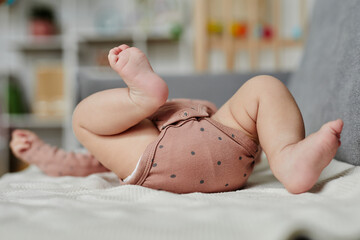 Close up of newborn in cotton bodysuit lying on back on sofa moving feet