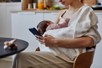 Cropped shot of woman with phone and newborn in white blanket resting after feeding, copy space