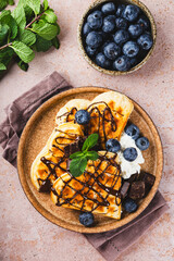 Homemade waffles with blueberries, chocolate sauce and cream cheese in a plate and a beige background top view vertical photo