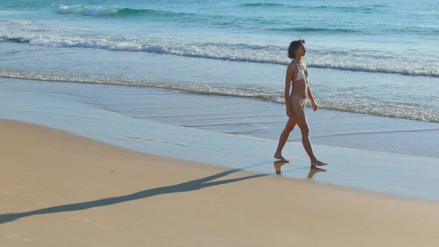 A young woman in a swimsuit walks along a sandy beach.
the girl walks slowly along the beach and enjoys her vacation. silhouette of a young girl on the beach.