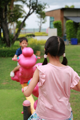 Asian child playing on toy seesaw toy in garden. Focus at the back of girl.