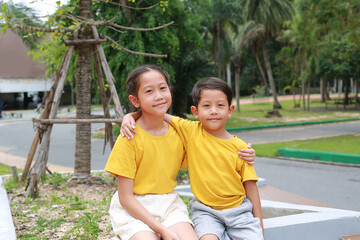 Obraz premium Happy Asian young girl child and little boy kid hug the neck and smile. Portrait Caucasian little brother and older sister hugging or arms around each other's shoulders, outdoor. Sibling love.
