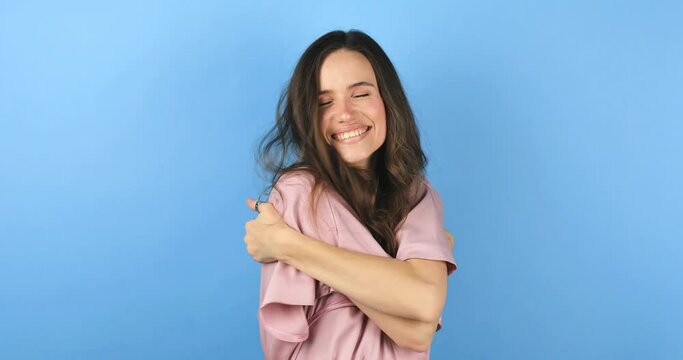 Come into my arms. Adorable happy girl with brown hair in pink dress gesturing come here for free hugs and smiling sincerely with welcoming expression isolated on blue background. Come to me, hug self