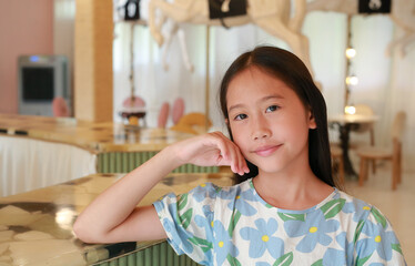 Portrait close-up of smiling Asian girl child hand touch cheek while sit on chair and lying at marble table with looking camera.