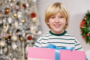 portrait of blond little boy smiling with decorated christmas tree on background