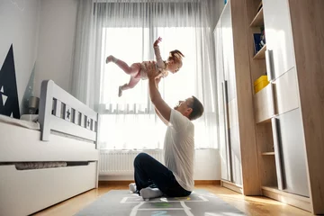 Fotobehang Father is sitting on the floor in nursery room and tosing his daughter in the air during their playtime. © dusanpetkovic1