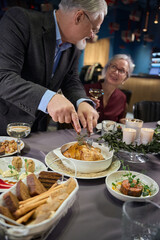 Aged man cutting roast meat for New Year celebrating with woman in restaurant