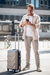 Handsome man with suitcase using smartphone browsing Internet on cellphone.
