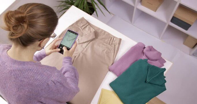 A woman selects clothes to donate and takes photos with her smartphone before sending them. Donation or recycling concept.