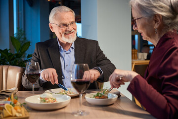 Smiling aged man and woman eating festive dinner during New Year celebration