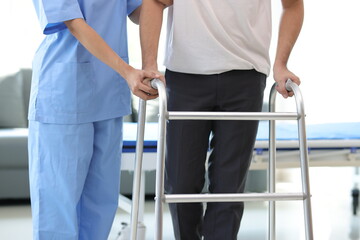 Female doctor helps a male patient who is in physical therapy and is practicing walking with a cane.