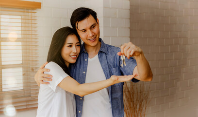 Handsome Asian couple and a beautiful, happy new home owner look at the keys in their hands with...