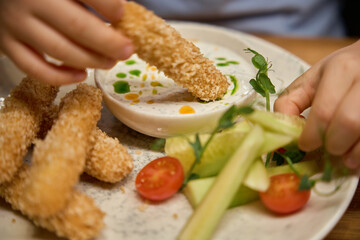 Unrecognizable child eating nuggets with sauce on Christmas dinner in cafe