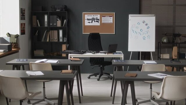 No people dolly in of empty military academy class with with two rows of desks and professor table beside flipchart and military related equipment
