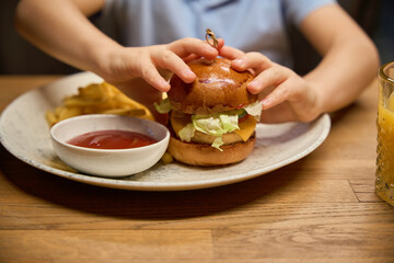 Unrecognizable child taking burger in restaurant during winter holidays