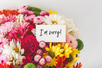 bright multi-colored bouquet of flowers with white card with the inscription i am sorry, the...