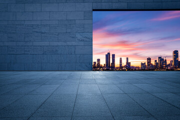 Empty square floor and brick wall with city skyline at sunset