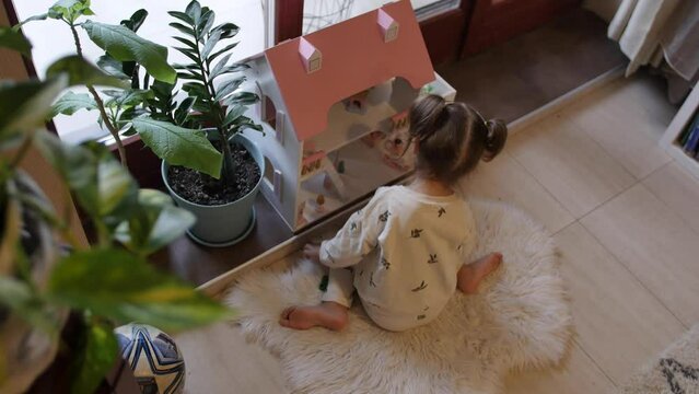 The little girl enjoys playing at home with her favorite dolls and toy dollhouse
