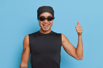 Sportive man with gogles on his face posing on blue background with thumb up, sport life concept, copy space