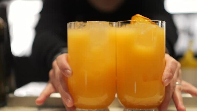 Barman porge due bicchieri con cocktail color arancio.
Primo piano sul bicchieri dell'aperitivo.