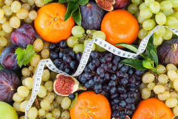 Naklejka na ściany i meble Diet concept with measuring tape, orange tangerine, figs and grape fruit mix with green leaves. Healthy food background