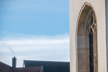 Schrägansicht eines gotischen Kirchenfensters vor unscharfem Hintergrund Dächer mit rauchendem...