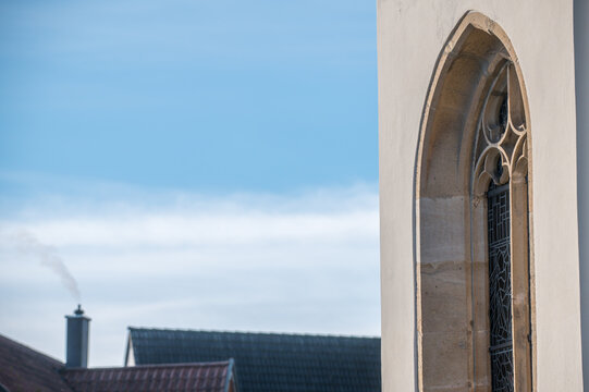 Schrägansicht eines gotischen Kirchenfensters vor unscharfem Hintergrund Dächer mit rauchendem Schornstein