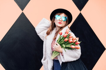 Happy emotional young fashion woman in heart-shaped sunglasses holding bouquet of fresh tulip...