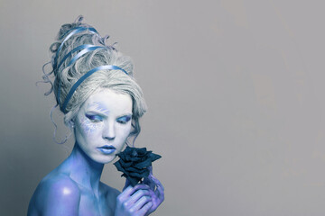 Portrait of a perfect woman with fantasy makeup and dark blue rose flower on grey background