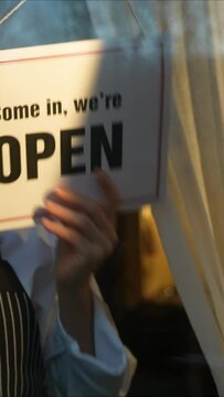 Vertical video of business owner attractive woman turning CLOSED sign to OPEN sign on front door smiling welcoming clients to cafe.
