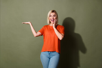 Photo portrait of lovely young lady excited palm hold empty space wear trendy orange garment isolated on khaki color background