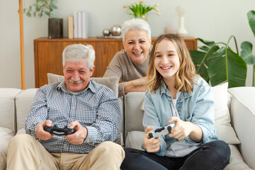 Happy family at home. Old senior man grandfather woman grandmother girl granddaughter playing video game with joysticks at home. Grandparent teenager two generations using gamepads for video game