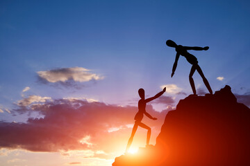 Two silhouettes mannequin climb mountain, one helping other, extending helping hand. Against...