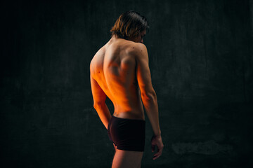 Fototapeta na wymiar Healthy fit relief ack. Rear view of young shirtless man with muscular body standing in underwear against dark textured studio background. Concept of men's beauty, health, body art and aesthetics