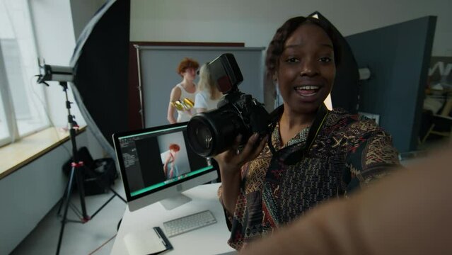 POV shot of African American female photographer holding professional camera and telling about fashion photo shoot process in studio