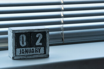 Morning January 02 on wooden calendar standing on window with blinds.