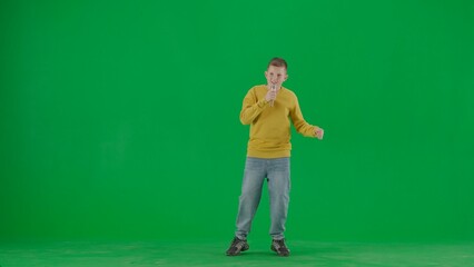 Portrait of kid boy on chroma key green screen. Schoolboy in jeans holding holding karaoke microphone and singing song. Full body front shot.